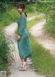 A woman in a green dress standing on a dirt road.