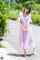 A woman in a purple dress standing on a sidewalk.