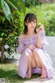 A woman in a purple dress sitting on the ground holding a flower.