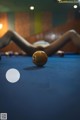 A woman laying on a pool table next to a pool ball.