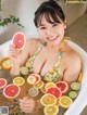 A woman in a bathtub holding a slice of grapefruit.