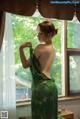 A woman in a green dress standing by a window.