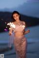 A woman in a pink dress holding sparklers on the beach.