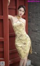 A woman in a yellow dress leaning against a red wall.