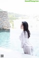 A woman in a white dress sitting by a swimming pool.