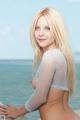 A woman in a white top is posing by the ocean.